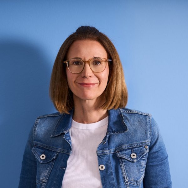 Frau steht mit Jeansjacke und T-Shirt vor blauer Wand